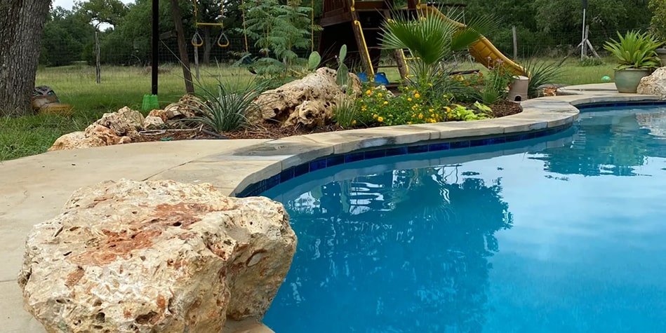 pool seen with a large bolder and cacti garden seen nearby with a playground seen in the background
