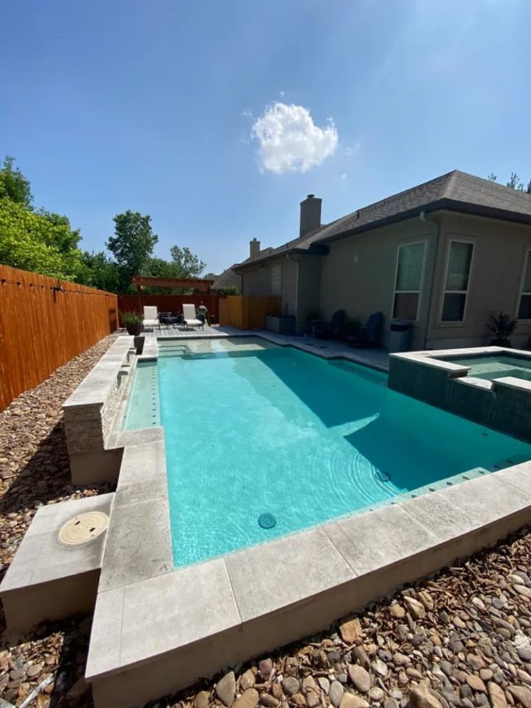 pool area seen on the side of a house with the house and fence seen in the background.