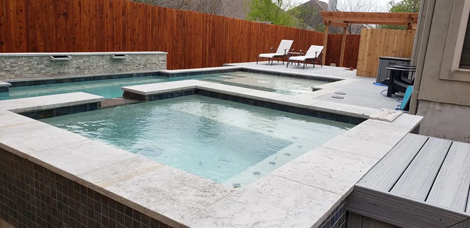 Hot tub seen with pool, chairs, and fence in the background.