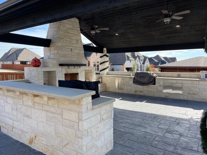 Covered patio area with grills, fireplace, and fans in a large stone area.